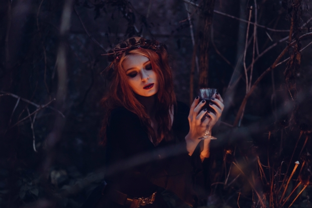 A beautiful witch holds a cup of wine in the dark woods